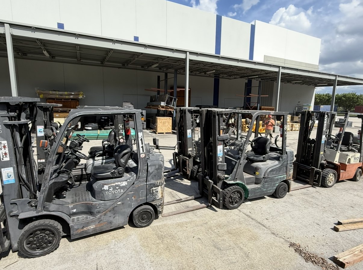 Fleet of used Toyota and Nissan cushion-tire forklifts staged under a loading dock canopy for fleet liquidation