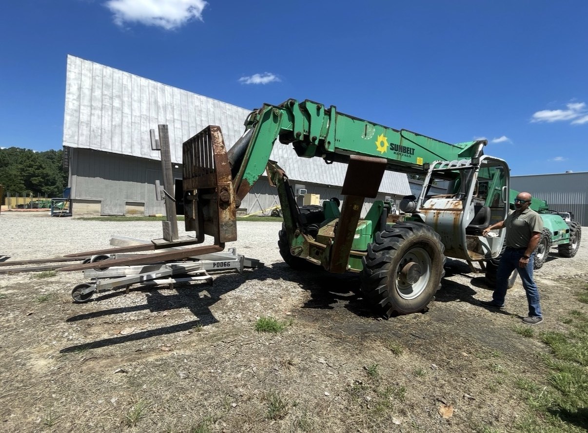 Green telehandler being inspected by a buyer on a gravel lot, boom lowered with forks forward